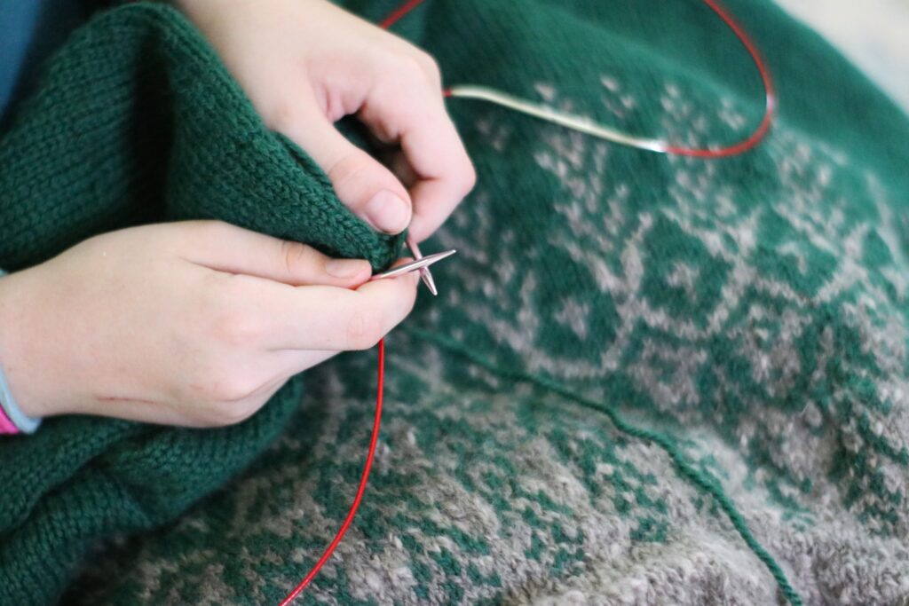 hands knitting a green and gray colorwork sweater