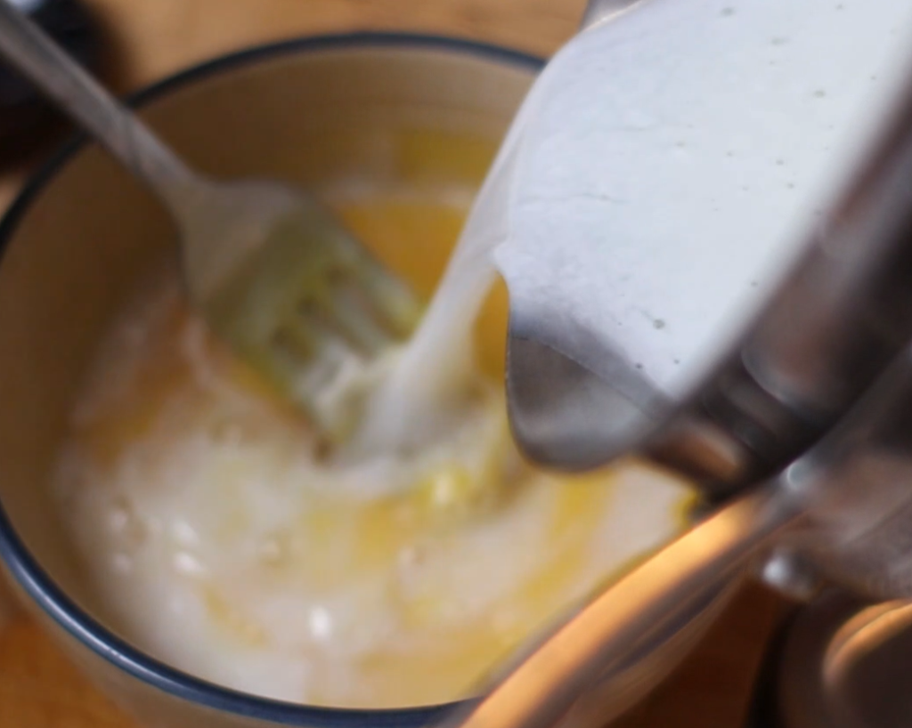 pouring a hot milk and sugar mixture into a bowl of egg yolks.