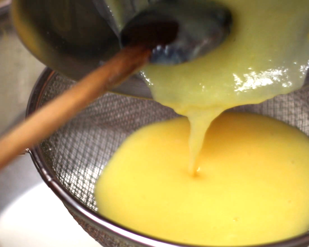 pouring custard through a strainer into a bowl of cream