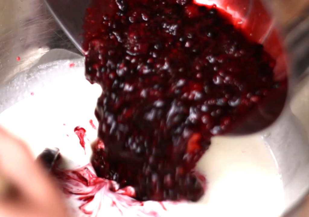 pouring crushed blackberries into cream