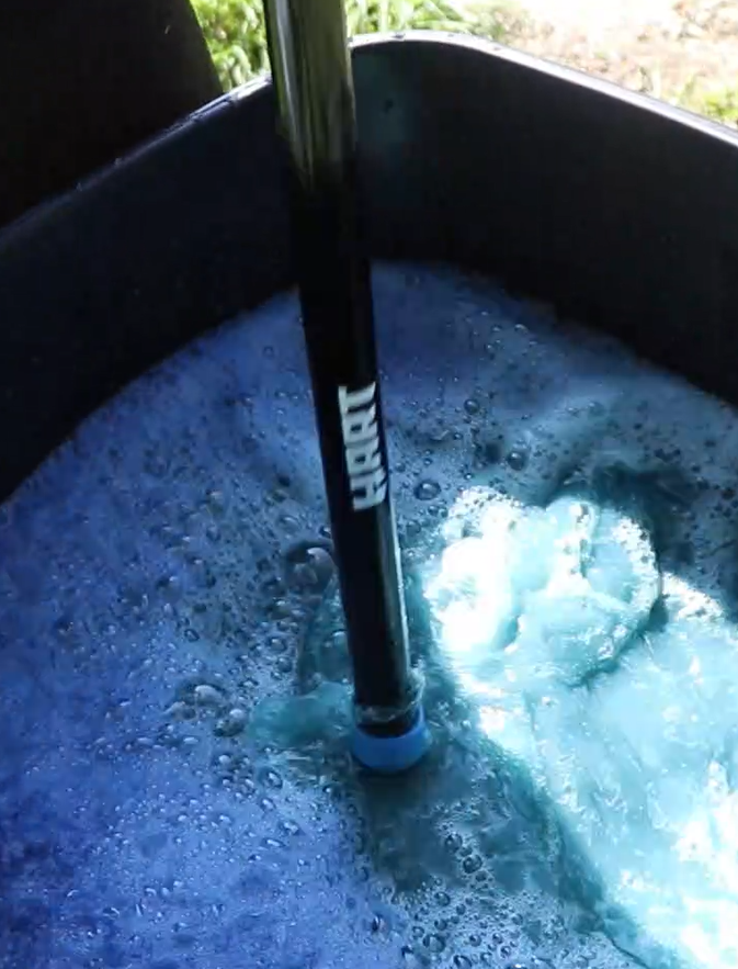 a bin of frothy blue water, with a black rake sticking out of it.