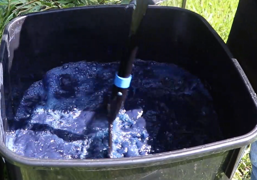 a bin full of deep blue water, being stirred by a rake