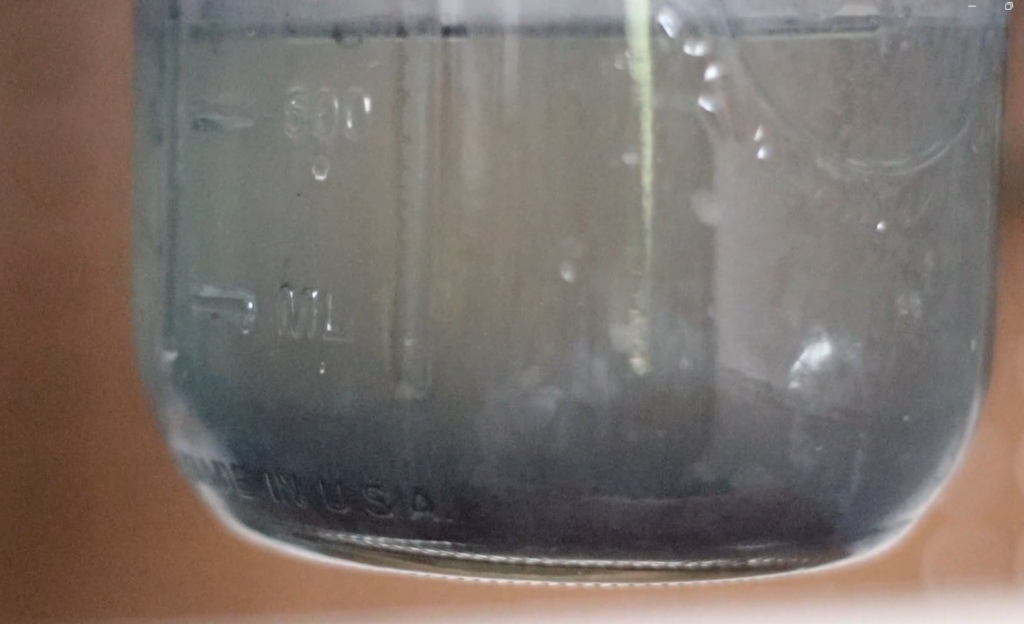 a jar of clear water with dark blue indigo pigment granules on the bottom.