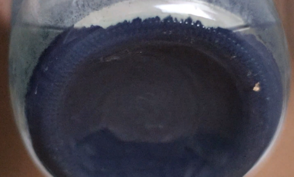 the bottom of a glass jar. dark blue indigo pigment granules cover the bottom of the jar.