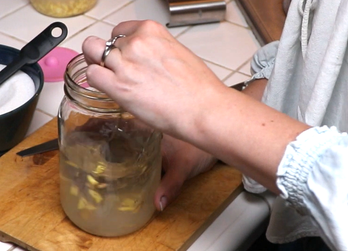 how to make a ginger bug hands stirring a jar full of water, chopped ginger, and sugar.