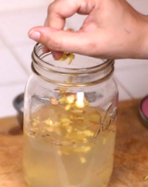 a hand putting chopped ginger into a gar to make a ginger bug