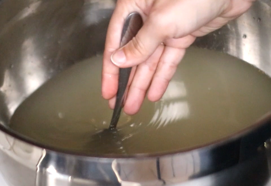 a hand stirring ginger beer in a bowl