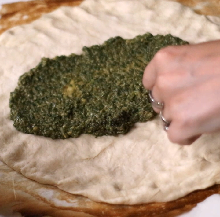 spreading pesto on pizza dough
