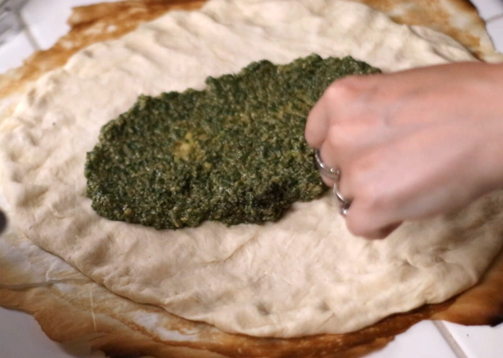 spreading pesto on pizza dough