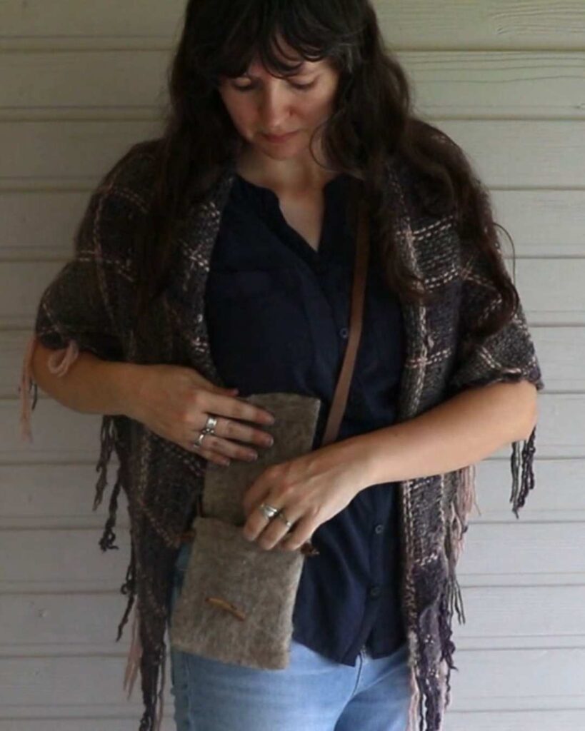 a woman wearing a woven plaid shawl, and a finished wet felted rustic bag with a leather strap