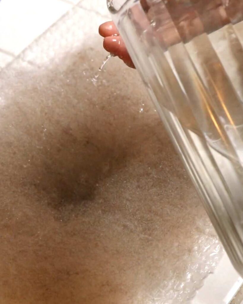 hands dribbling hot water onto a layer of wool, in order to create felt