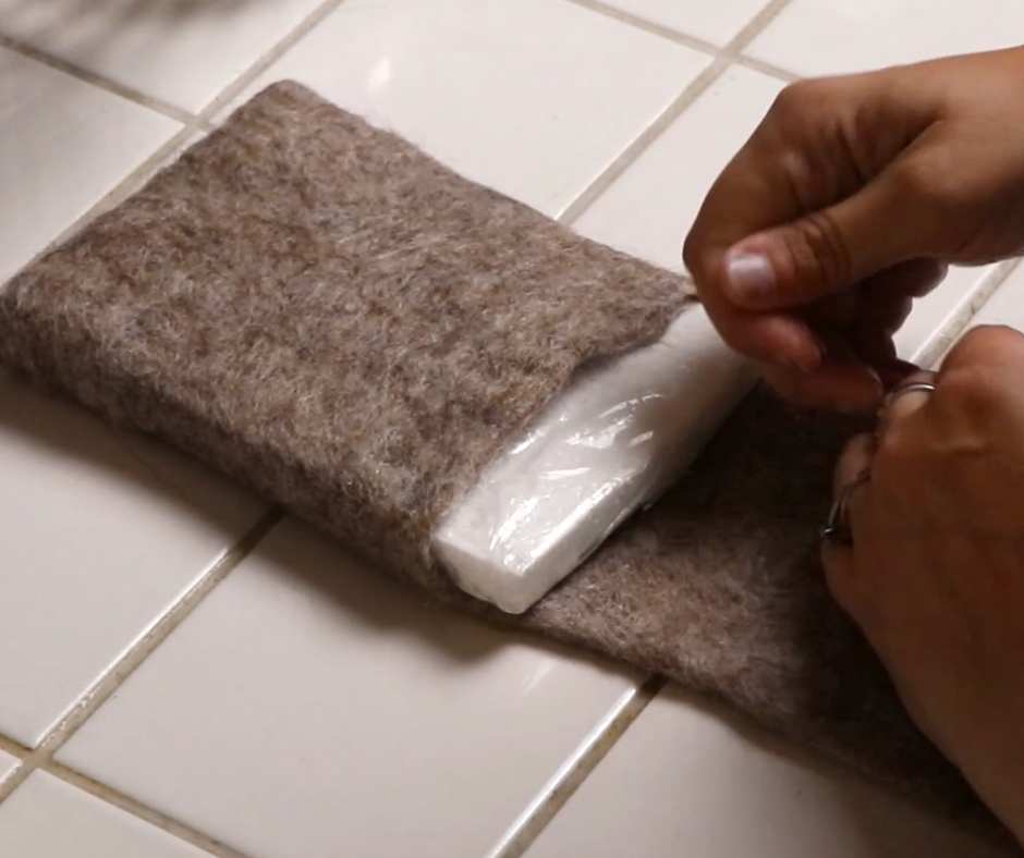 hands inserting a styrofoam form into a wet felted bag, to create shape while the bag dries