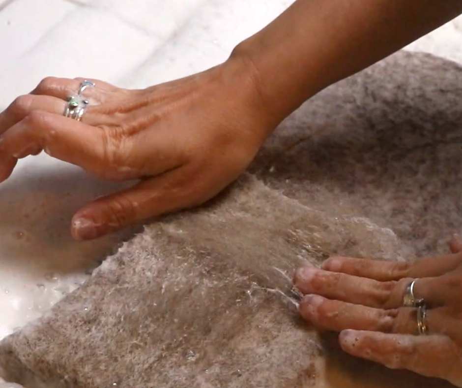 hands adding a few tufts of wool onto a wet felted bag, in order to reinforce thing spots