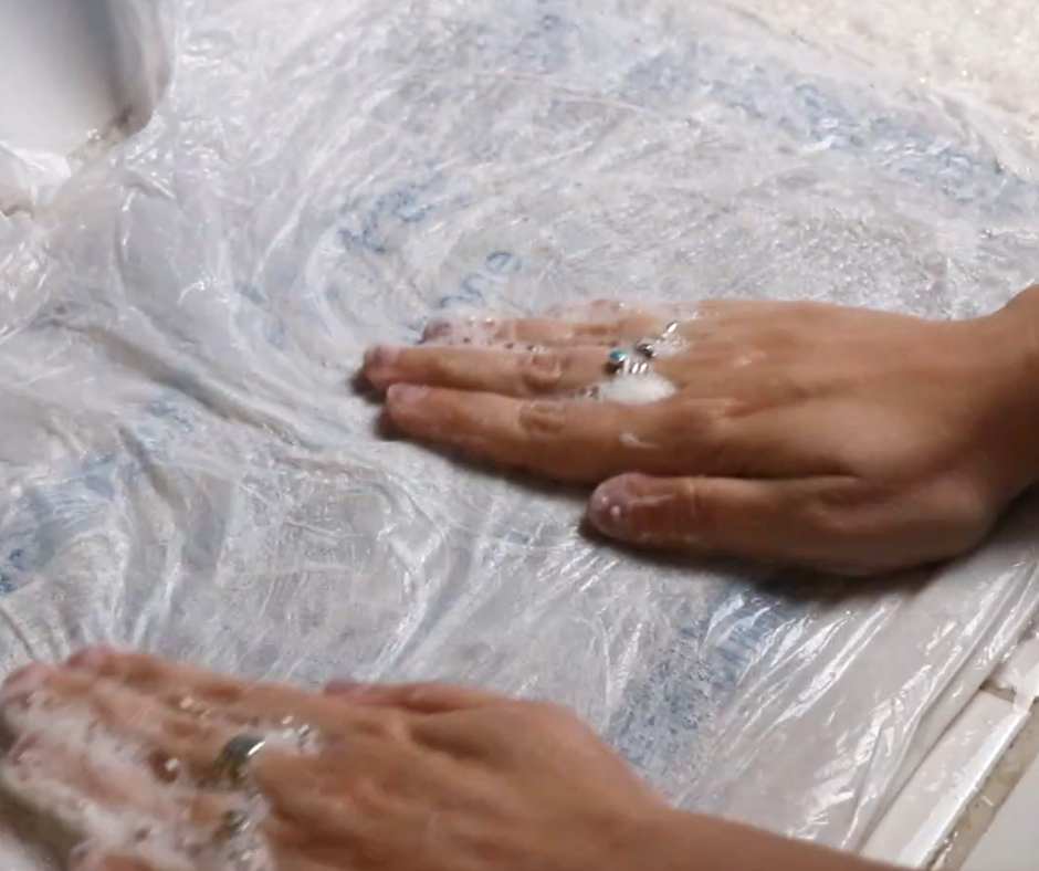 hands rubbing a layer of thin plastic covering a layer of wool, with soap and water all over it, in order to create felt