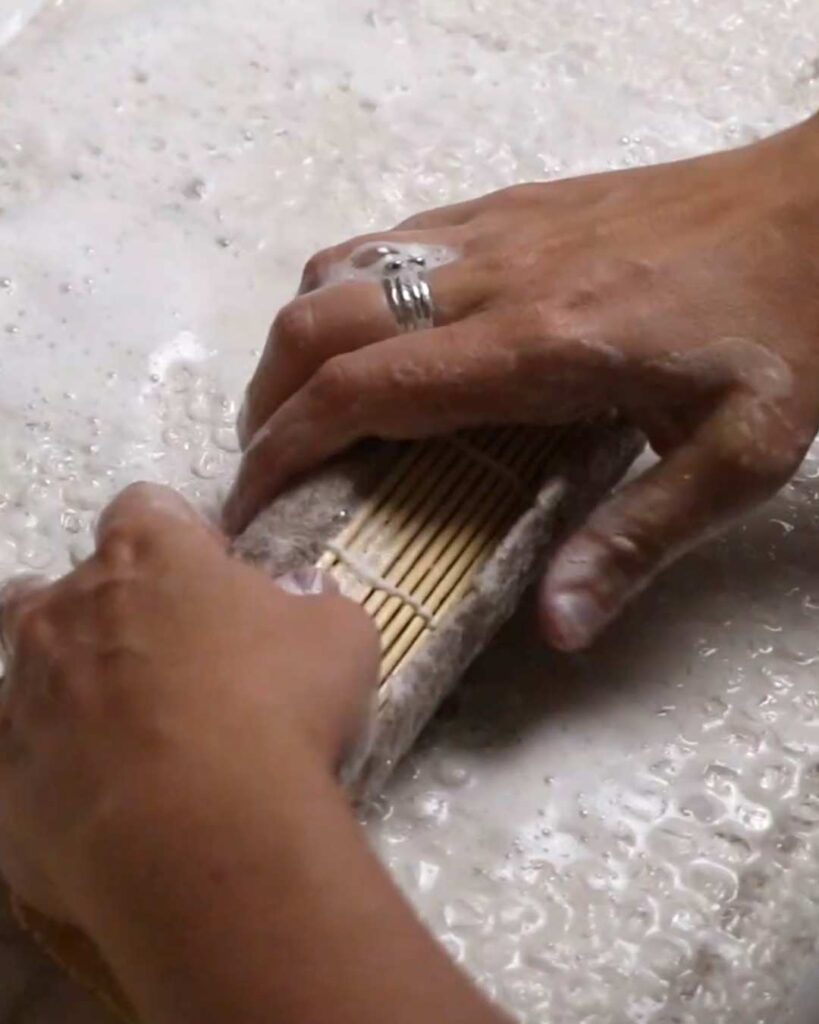 hands using a bamboo mat to roll wet felt in order to compress and strengthen it