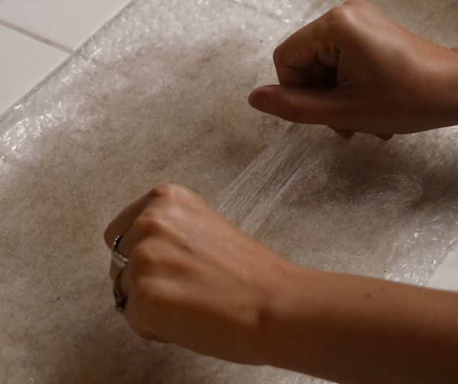 hands carefully placing a tuft of wool onto a layer of wool, in order to create felt