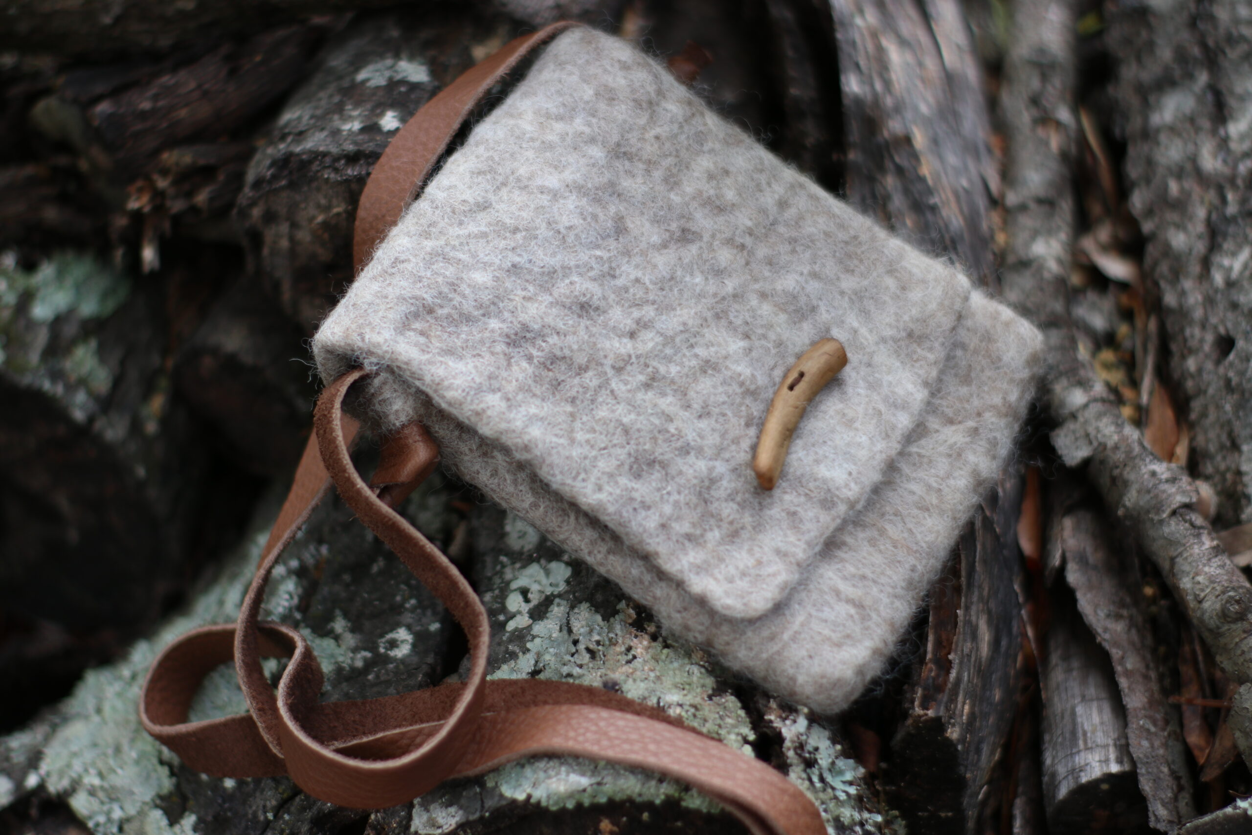 a rustic gray wet felted wool bag, with a wooden button and leather strap.