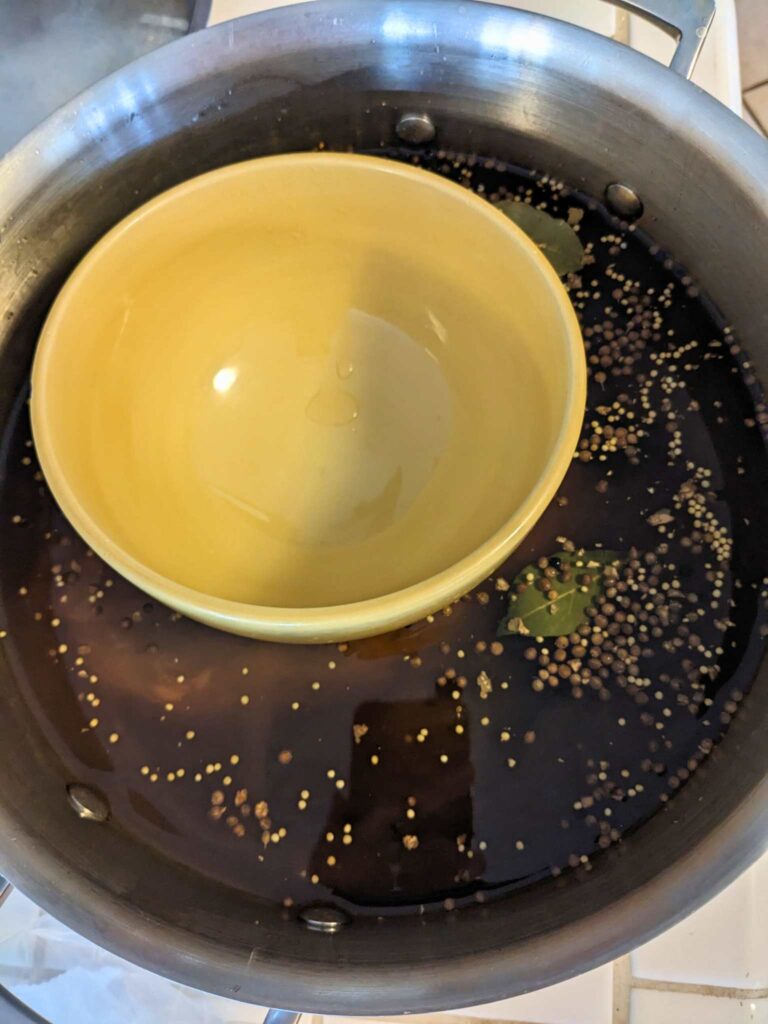 a bowl being used to weigh down venison roast in a pot of brine