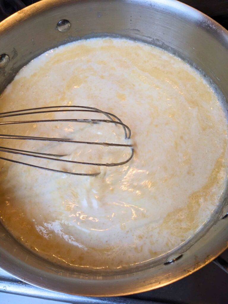 whisking milk into the roux to make creamed eggs on toast