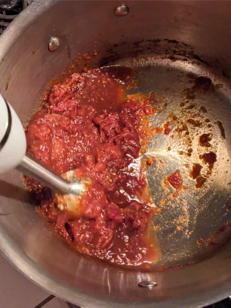 using an immersion blender to puree homemade tomato sauce