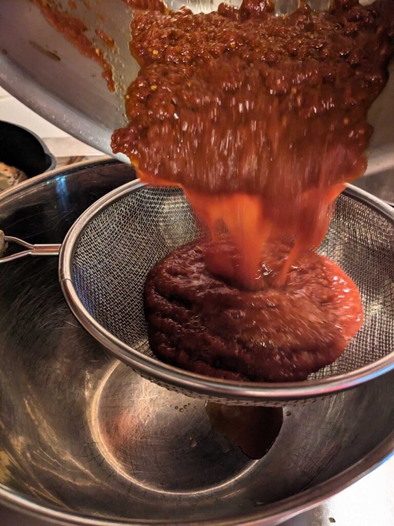 using a strainer to remove peels and seeds from homemade tomato sauce