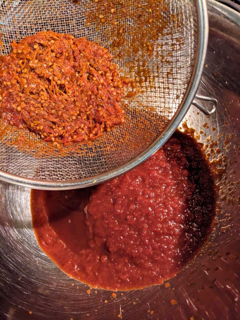 using a strainer to remove peels and seeds from homemade tomato sauce