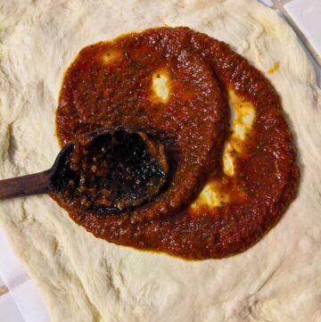 smearing homemade tomato sauce onto pizza dough with a wooden spoon