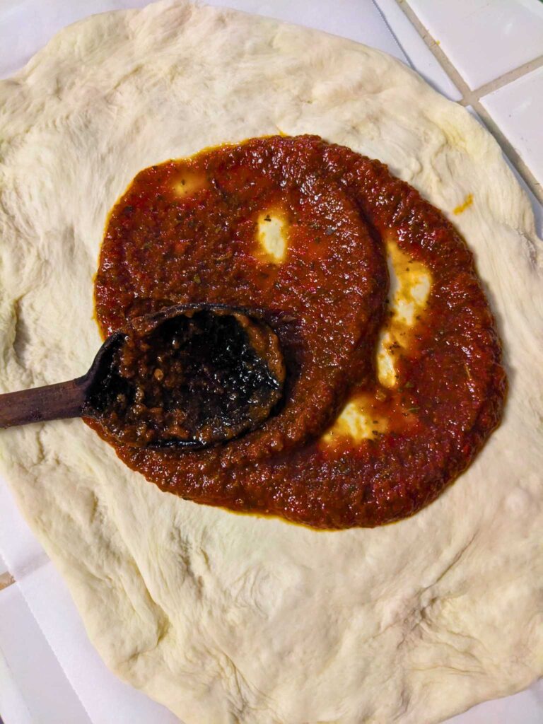 smearing homemade tomato sauce onto pizza dough with a wooden spoon