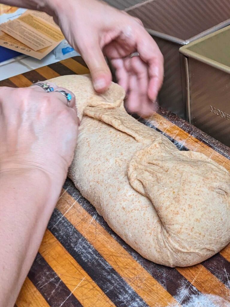 stretching the sides of the bread dough log into the center