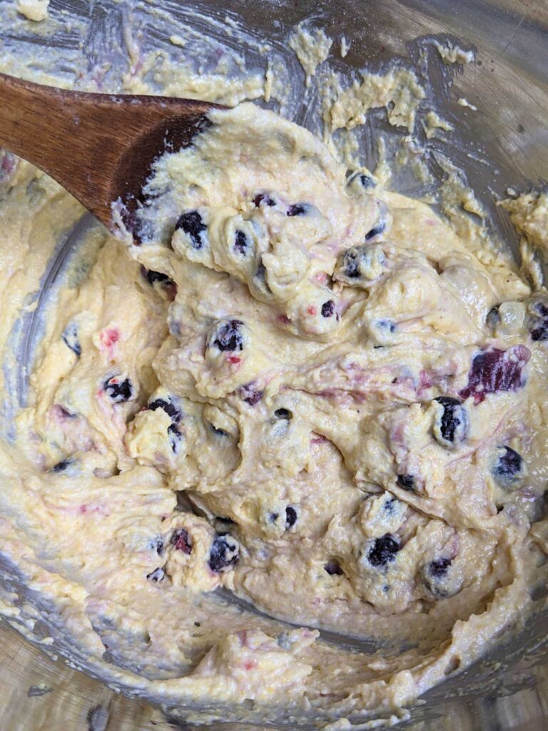 folding blueberries into cornbread batter with a wooden spoon