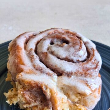 a whole wheat cinnamon roll with glazed frosting, on a blue plate.