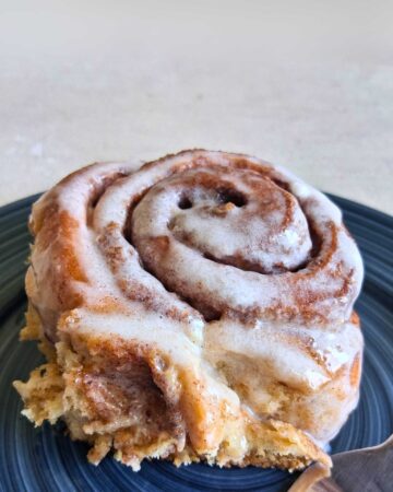 a whole wheat cinnamon roll with glazed frosting, on a blue plate.