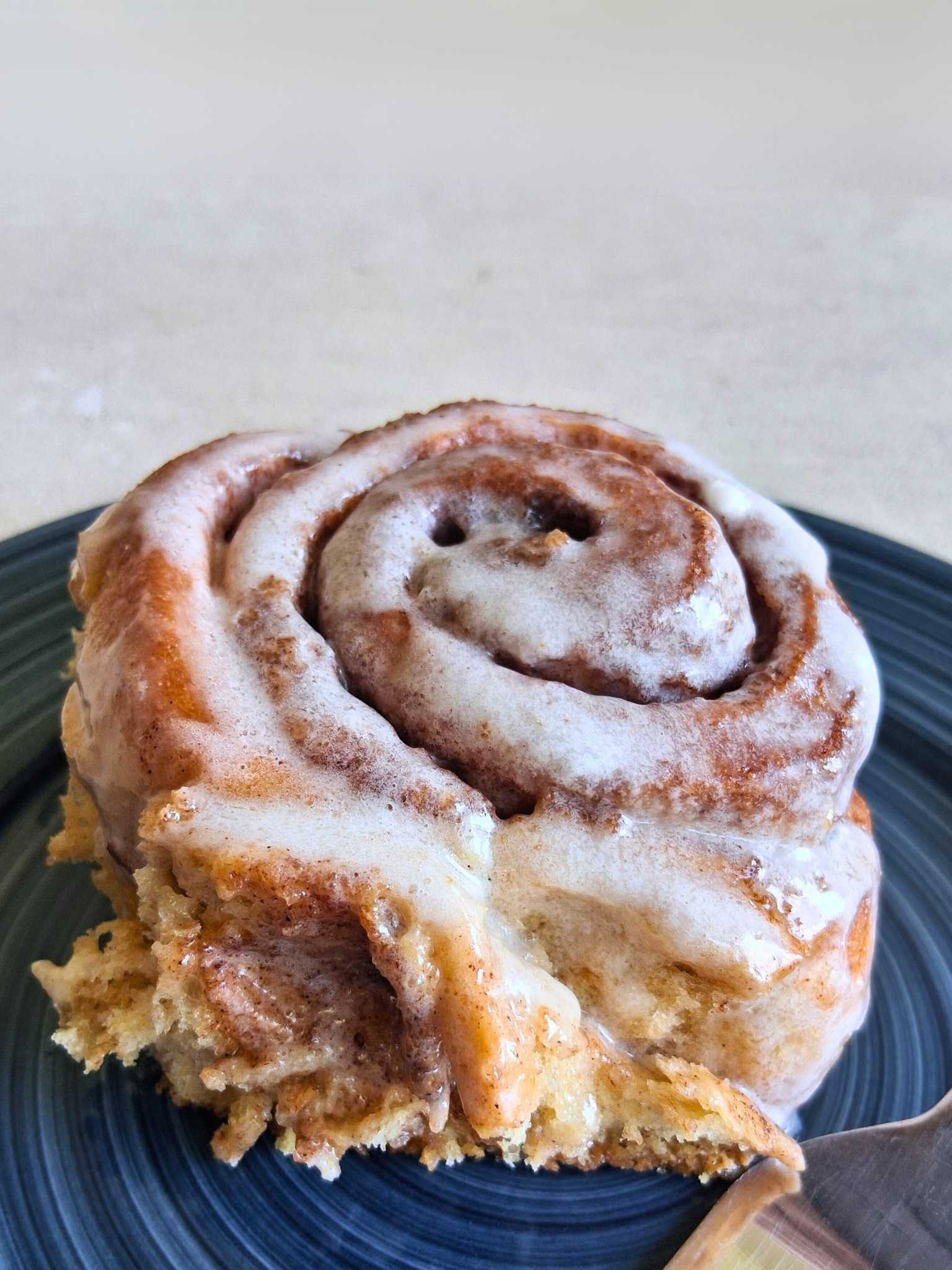 a whole wheat cinnamon roll with glazed frosting, on a blue plate.