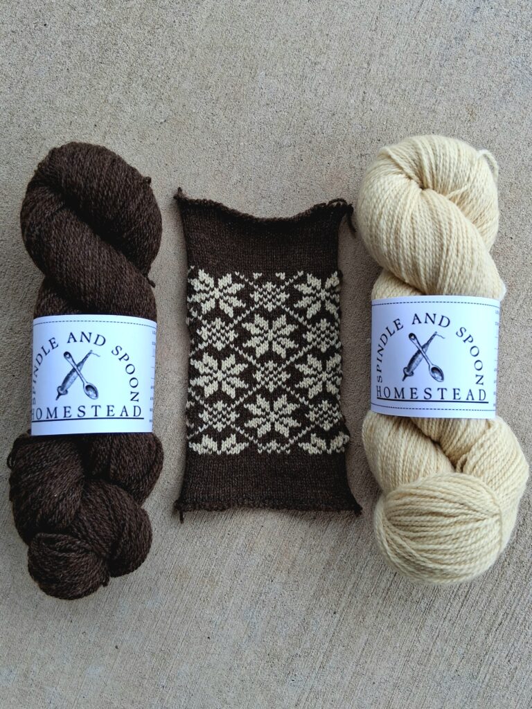 a skein of brown yarn, and a skein of off-white yarn, with a knitted sample in between them featuring a snowflake pattern.